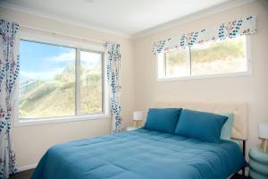a bedroom with a blue bed and two windows at Hilltop Ocean Hideaway - Aotea Wellington in Porirua