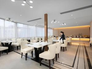 a woman standing in a restaurant with tables and chairs at Vienna Hotel Yongzhou Dong'an High-Speed Railway Station in Guzhuting