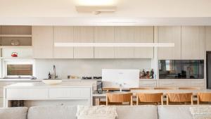 a kitchen with white cabinets and a table and chairs at Pearl On The Beach By Holidayco in Umina