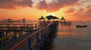 a pier with a boat on the water at sunset at Hotel Dafam Pacific Caesar in Surabaya