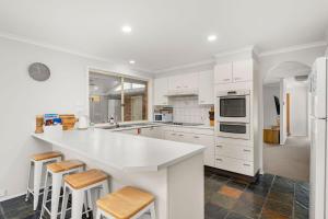eine Küche mit weißen Schränken und einer großen Insel mit Hockern in der Unterkunft The Quay To Sussex in Sussex inlet