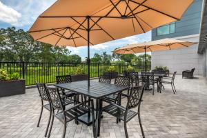 タンパにあるCambria Hotel Tampa-Brandonのテーブルと椅子、パラソルのあるパティオ