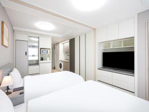 a white bedroom with a bed and a television at Elmomento Sasang in Busan