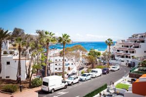 een stadsstraat met geparkeerde auto's en palmbomen bij Los cristianos Vistas al mar y cerca de la playa in Los Cristianos
