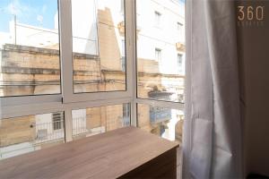 a window with a wooden table looking out at a building at Seaside Comfort in St'Pauls Bay steps from the Sea by 360 Estates in St Paul's Bay