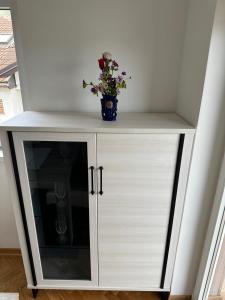 un armario blanco con un jarrón de flores. en studio apartman elegant marinkovic, en Vrnjci