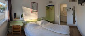 Una pequeña habitación con una cama, una mesa y una ventana. en Fasthotel Well Inn Mâcon sud - un hôtel FH Confort, en Charnay-lès-Mâcon