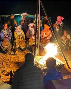 a group of people sitting around a fire at Merzouga Hamza Luxury Camp in Merzouga