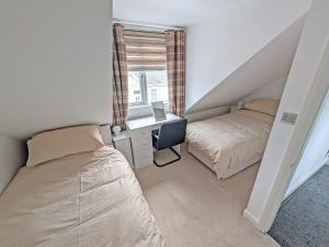 a bedroom with two beds and a desk and a window at Greens Cottage in Girvan