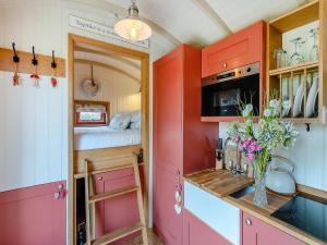 a small kitchen with red cabinets and a bed at Bonnie's Shepherd Hut - Uk50228 in Nottingham