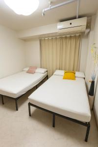 two beds in a room with white sheets and a yellow pillow at 1008 本町駅徒歩3分インペリアル快適ルーム 最大6名 in Osaka