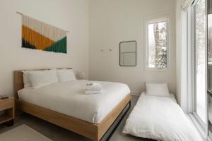 a white bedroom with two beds and a window at Woodland - Terrace - Fire pit - 15min Tremblant in La Conception