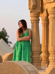 ジャイサルメールにあるRobins Desert Campの柱に寄りかかる緑のドレスを着た女性