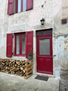 a red door and windows on a building with fire wood at Le Studio in Condeissiat