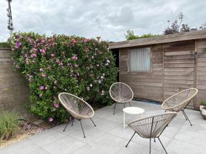 drie stoelen en een tafel en een struik met roze bloemen bij Vakantiehuisje Wenduine in De Haan