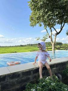 a young girl sitting on a wall next to a body of water at Villa Đăng HảI in Buôn Du Enguôl