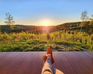 a person sitting on a wooden deck watching the sunset at Off-Grid Cabin Nestled Among Nature with Lovely Landscape Views in Maine in Lavertue