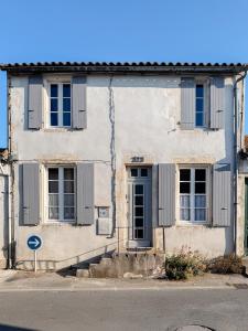 a white building with blue shutters on a street at L'Olivier de Milou in Le Bois-Plage-en-Ré