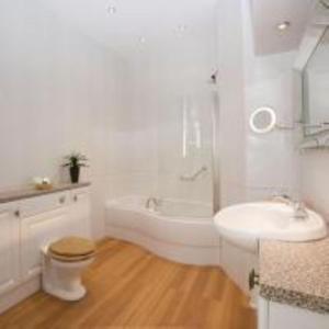 a white bathroom with a tub and a sink and a toilet at The George Hotel in Penrith