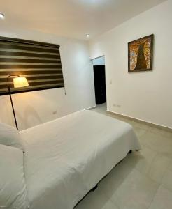 a white bedroom with a large bed and a lamp at Cozy Room in Monterrey
