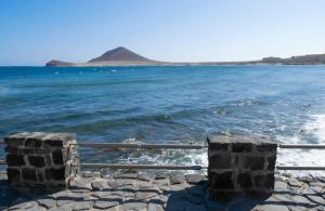 a fence next to the water with a mountain in the background at Casita Médano in El Médano