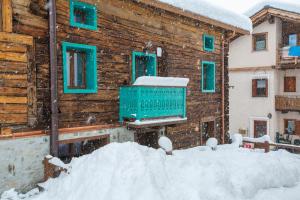 a wooden house with green windows and a pile of snow at Marlies Ski in - Ski out 50m - Happy Rentals in Livigno