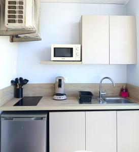 a kitchen with white cabinets and a sink and a microwave at Studio Le Sablé in Îlet à Christophe