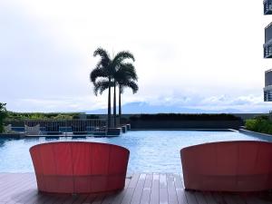 ein Schwimmbecken mit zwei roten Stühlen und einer Palme in der Unterkunft 90 Sqm Perfect Seaview Luxurious Modern 2 Bedrooms, Nearby Okada, Solaire, Airports, MOA with Free Parking in Manila