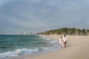 um homem e uma mulher caminhando na praia em Al Zorah Beach Resort em Ajman