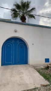 a blue door in a white building with a palm tree at Petite maison typique à 2 pas de la mer in Sousse