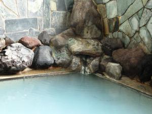 ein Wasserbecken in einer Steinmauer mit Felsen in der Unterkunft Ikemoto in Nozawa Onsen