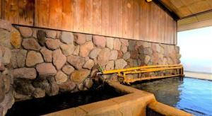a swimming pool with a stone wall and water at Yukemuri no sato azumaya in Beppu