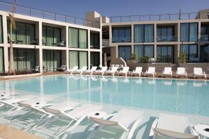 a swimming pool with white lounge chairs in front of a building at Inanna Resort in Batroûn