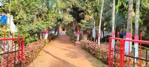 a dirt road with a red fence and trees at Deepdaya Cottage in Alībāg