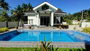 a villa with a swimming pool in front of a house at Teratak Nu'aiman With Pool in Bedung