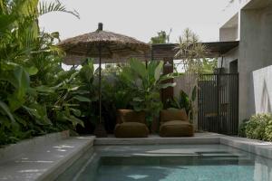 een zwembad met stoelen en een parasol naast een huis bij Tibah in Tanah Lot +16 foto's