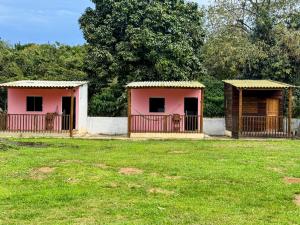 two small houses with gates in a grass field at Suítes Ohana in Peruíbe +3 photos