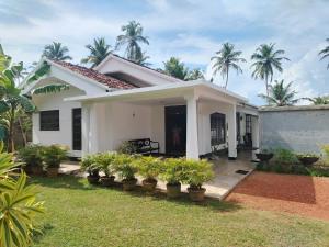 a white house with potted plants in a yard at Samudura Beach House, Owakanda in Rathgama