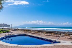 a swimming pool next to a beach with chairs and the ocean at Kulakane 310 · KK 310 Updated BeachFront 2BD w AC Pool in Kahana