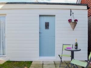 Un cobertizo blanco con una puerta azul y una mesa. en The Cabin, en Pevensey 4 fotos más