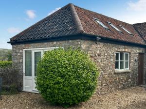 a stone house with a white door and a large bush at Noddingway Cottage in Weare