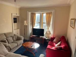 a living room with a red couch and a table at 1st Class Central 4 Bedroom 2 Bathrooms in Galashiels