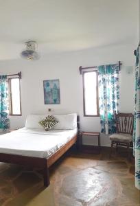 ein Schlafzimmer mit einem Bett und einem Stuhl und Fenstern in der Unterkunft Diani Gardens Cottage in Ukunda Airport