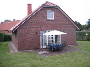 una casa de ladrillos rojos con una mesa y una sombrilla en ZeitVergessen, en Krummhörn