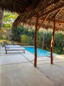 a bench under a straw umbrella next to a swimming pool at Villa Agay in Nosy Be