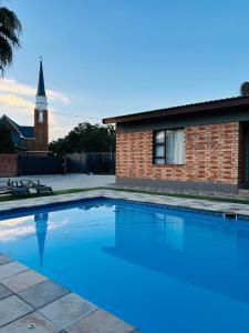 a swimming pool in front of a brick building with a clock tower at Hope Villa Luxury Accomodation in Odendaalsrus