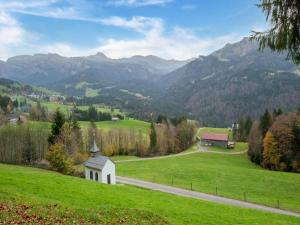 a green field with a church in the middle of a road at Dog-friendly holiday apartment in Bregenzerwald in Sibratsgfäll +22 photos