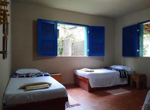 two beds in a room with blue shuttered windows at Casa Charme Jericó Guaramiranga in Guaramiranga