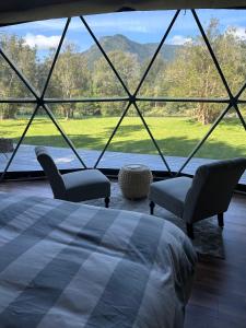 een slaapkamer met een bed en twee stoelen en een groot raam bij Alma Andina in Puelo