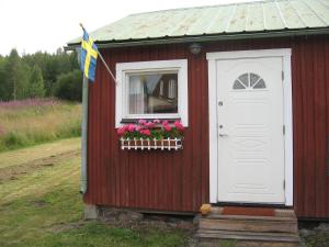 a red shed with a white door and flowers in a window at Lillvikens Gästhuset och Stugor in Nedre Lillviken